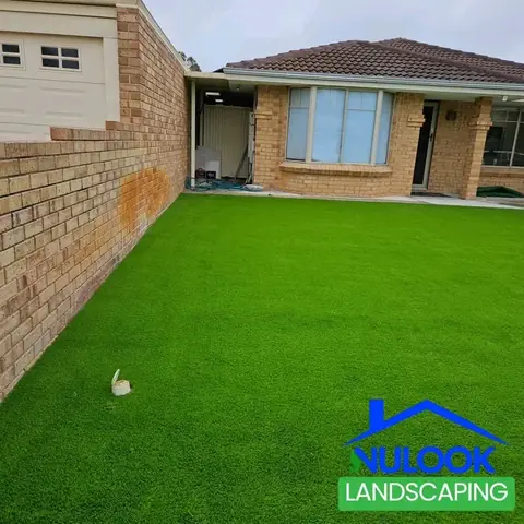 Front yard of a brick house covered in artificial grass, with a brick boundary wall on the left